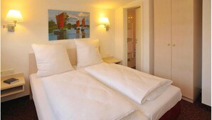 A hotel room with a double bed, two bedside lamps, a painting of a sailboat, and a wardrobe. - Hotel Blankenese (Hamburg)