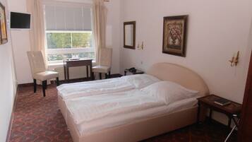 A hotel room with a bed, two chairs, a small table, a window with curtains, and a painting on the wall.