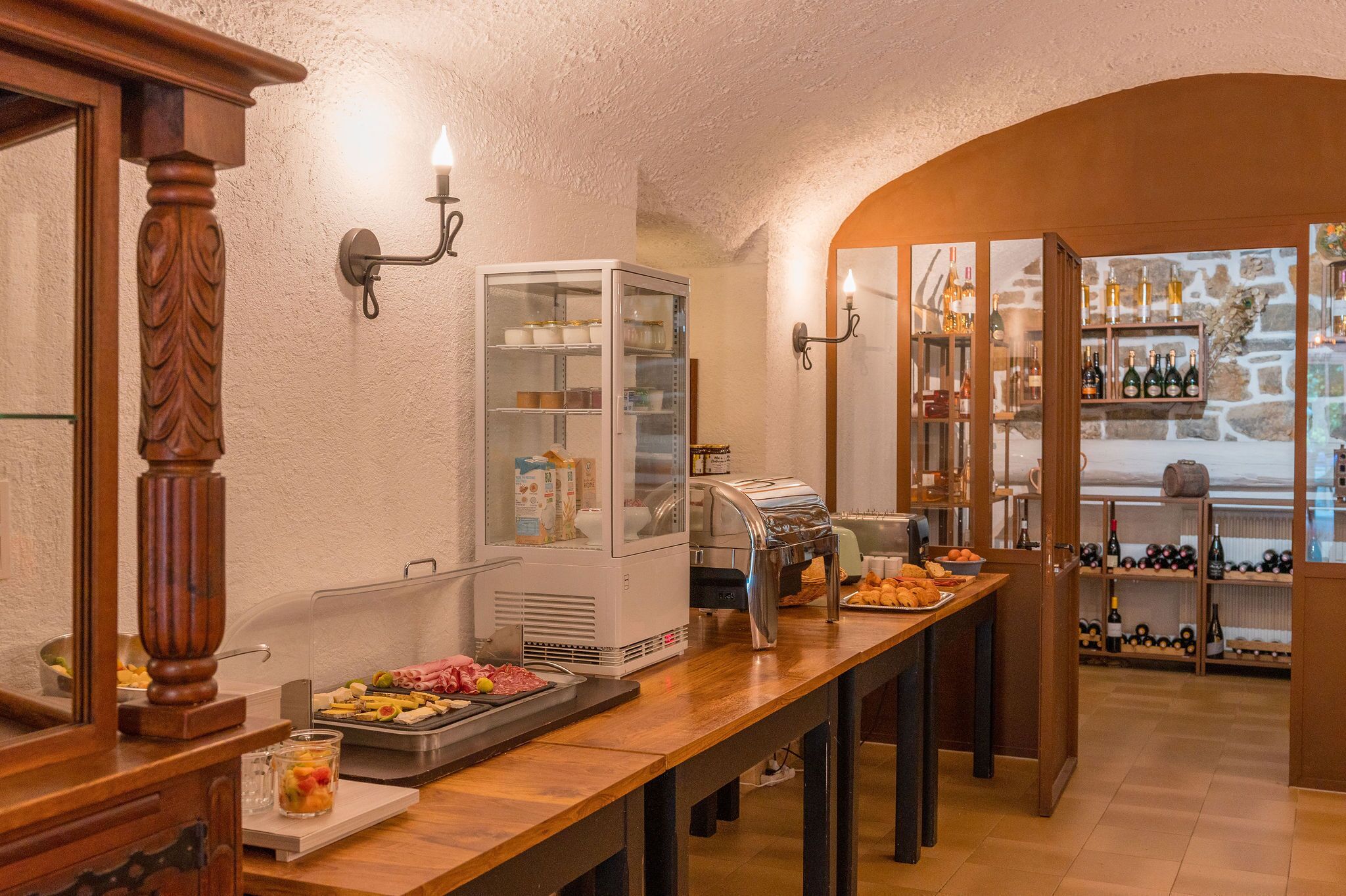 A buffet setup with a glass display case, a buffet station with food, and wine shelves.