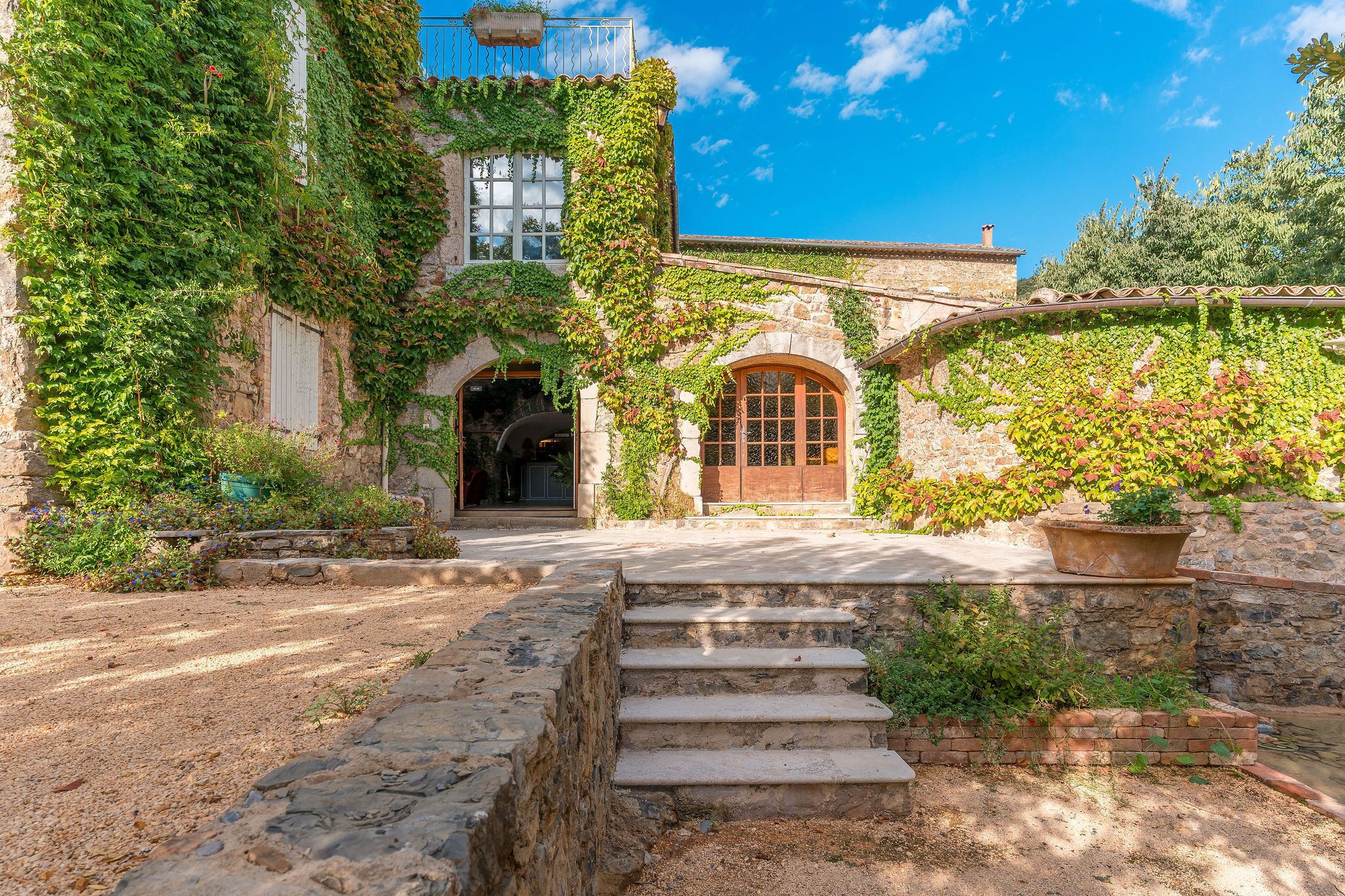 Un edificio de piedra con muros cubiertos de hiedra, una puerta de madera y una escalera de piedra que conduce a la entrada.