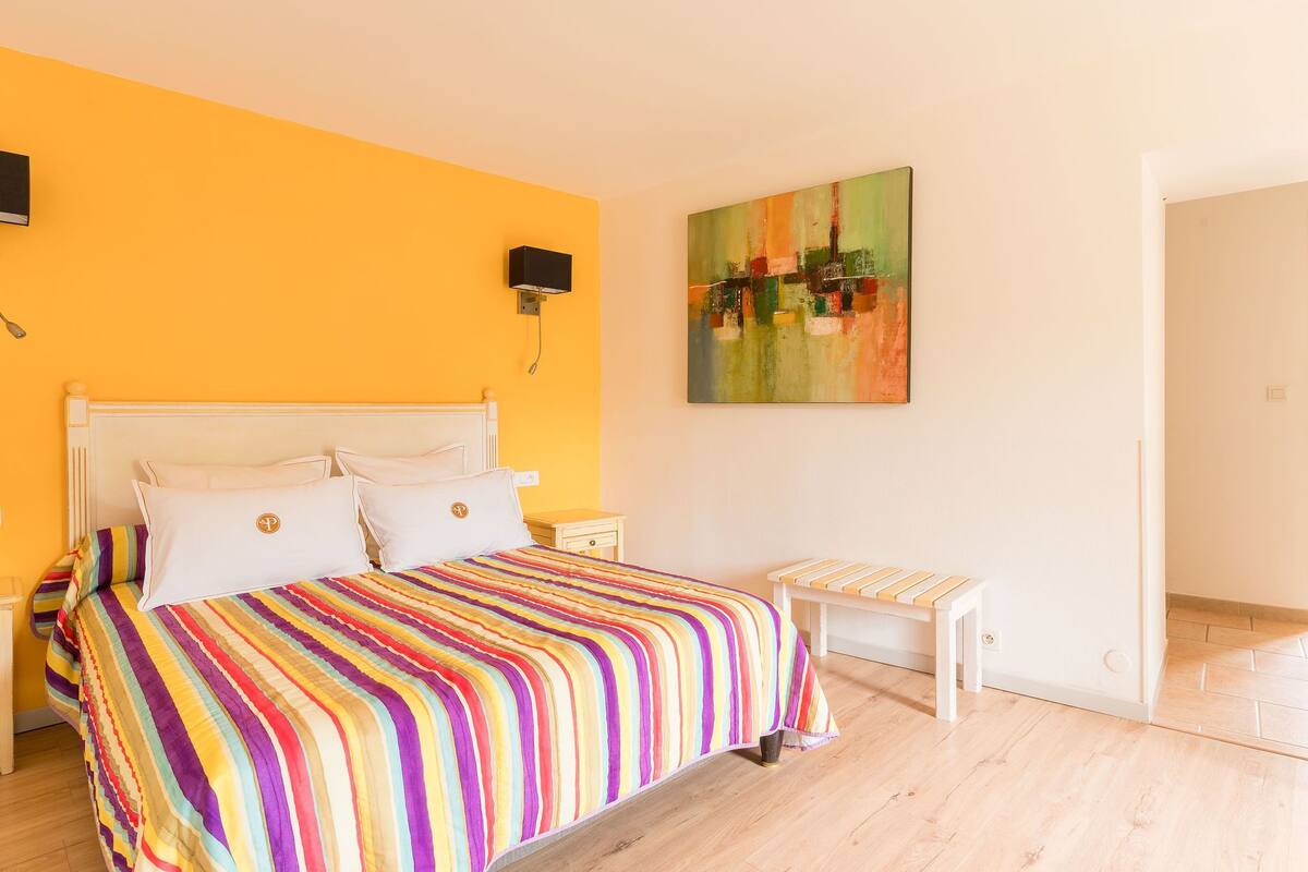Un dormitorio con cama, mesitas de noche, un banco y un cuadro en la pared.