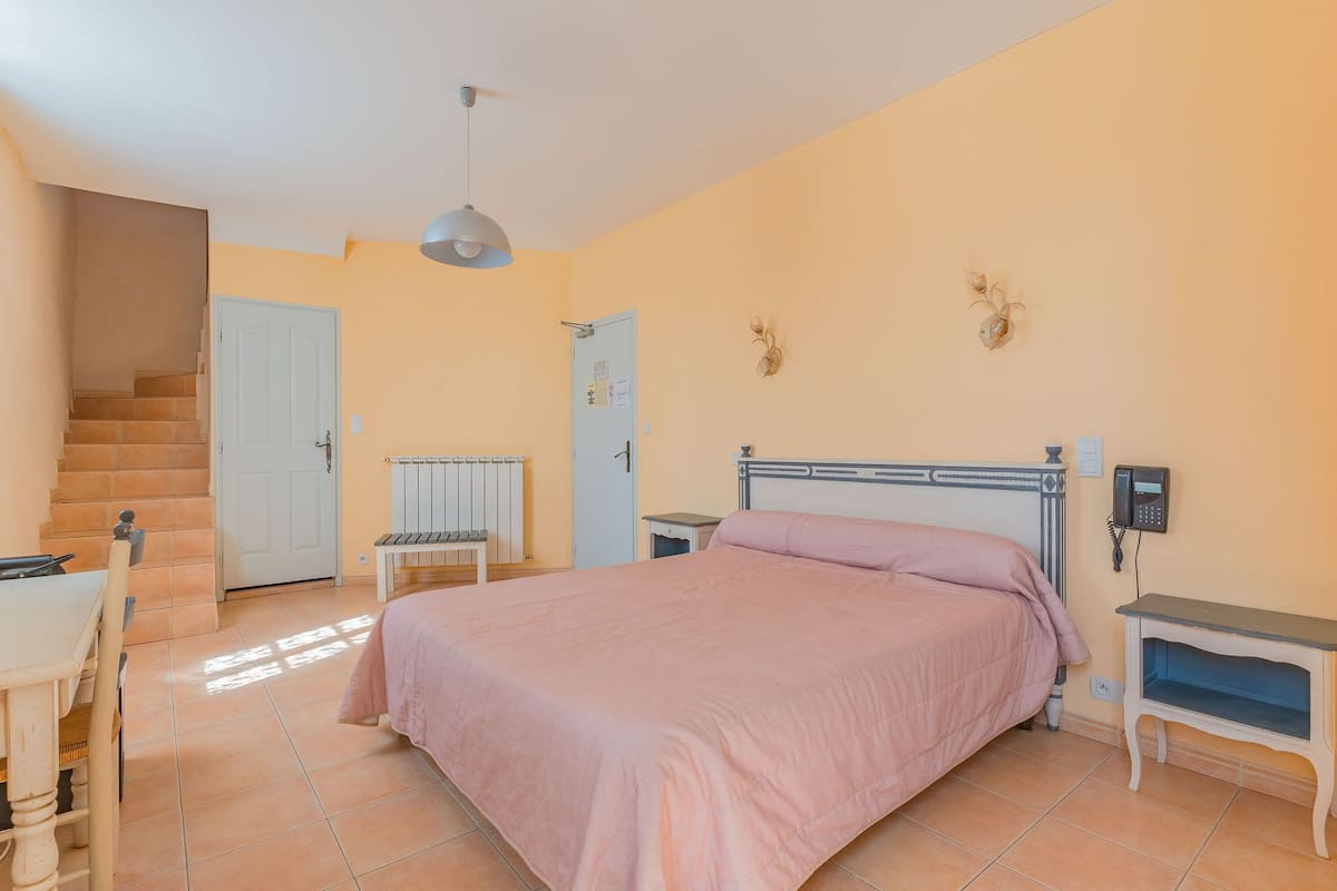Un dormitorio con cama, escritorio, silla, radiador, escalera y teléfono en la pared.