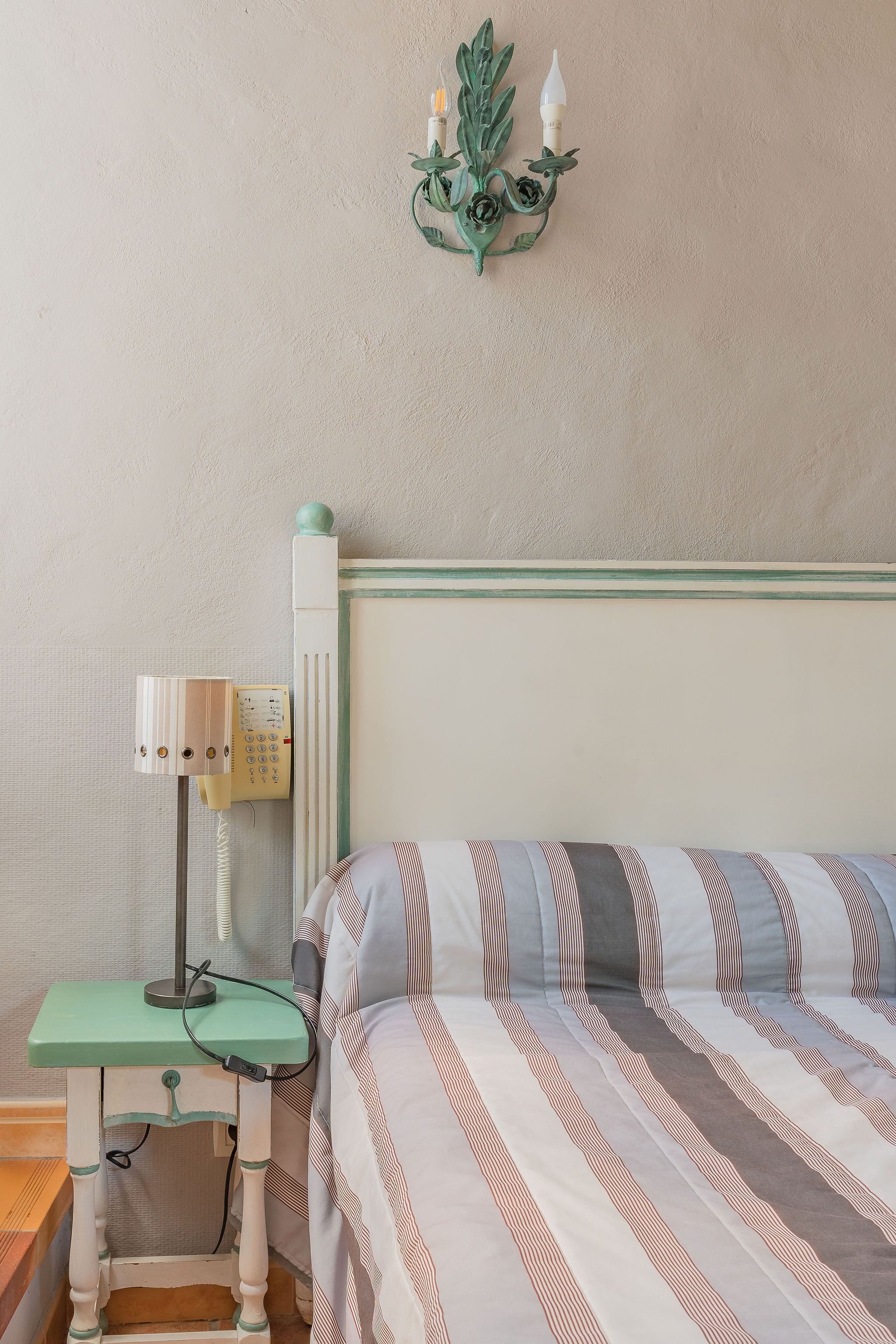 Una habitación con una cama, una mesita de noche con lámpara y una lámpara de pared.