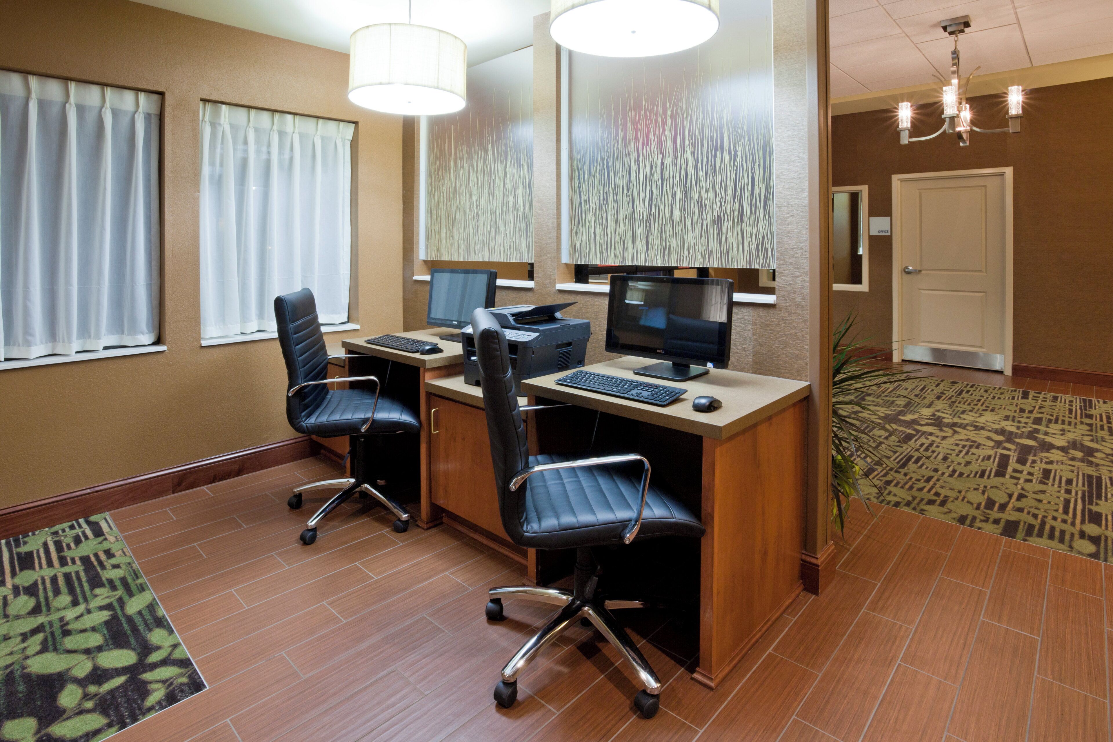 Un bureau d’hôtel avec deux bureaux, des chaises, des ordinateurs et un lustre.