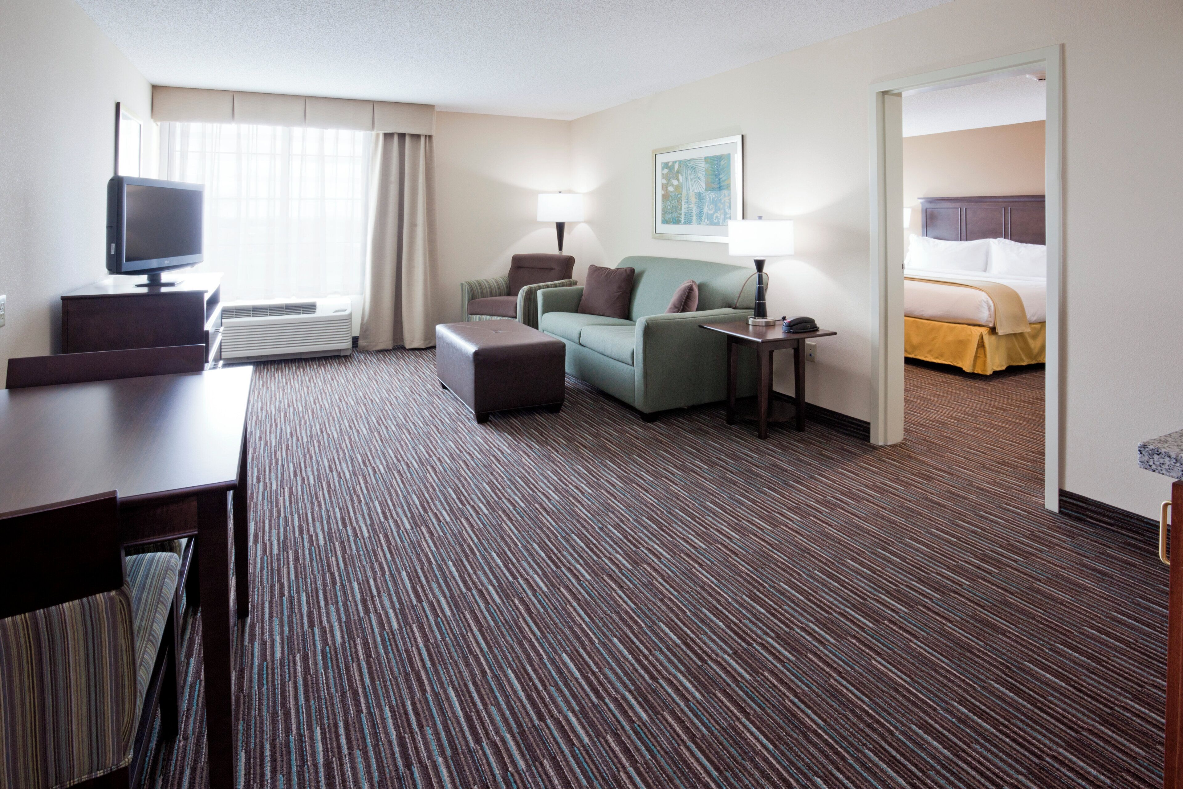 A hotel room with a flat-screen TV, a sofa, a small table, a lamp, and a bed.