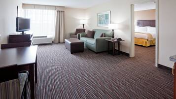 A hotel room with a flat-screen TV, a sofa, a small table, a lamp, and a bed.