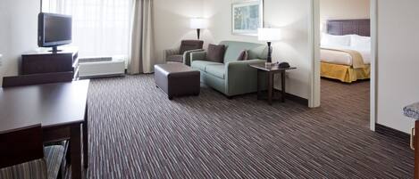 Ein Hotelzimmer mit Flachbildfernseher, einer Couch, einem Schreibtisch, einer Lampe und einem Bett.