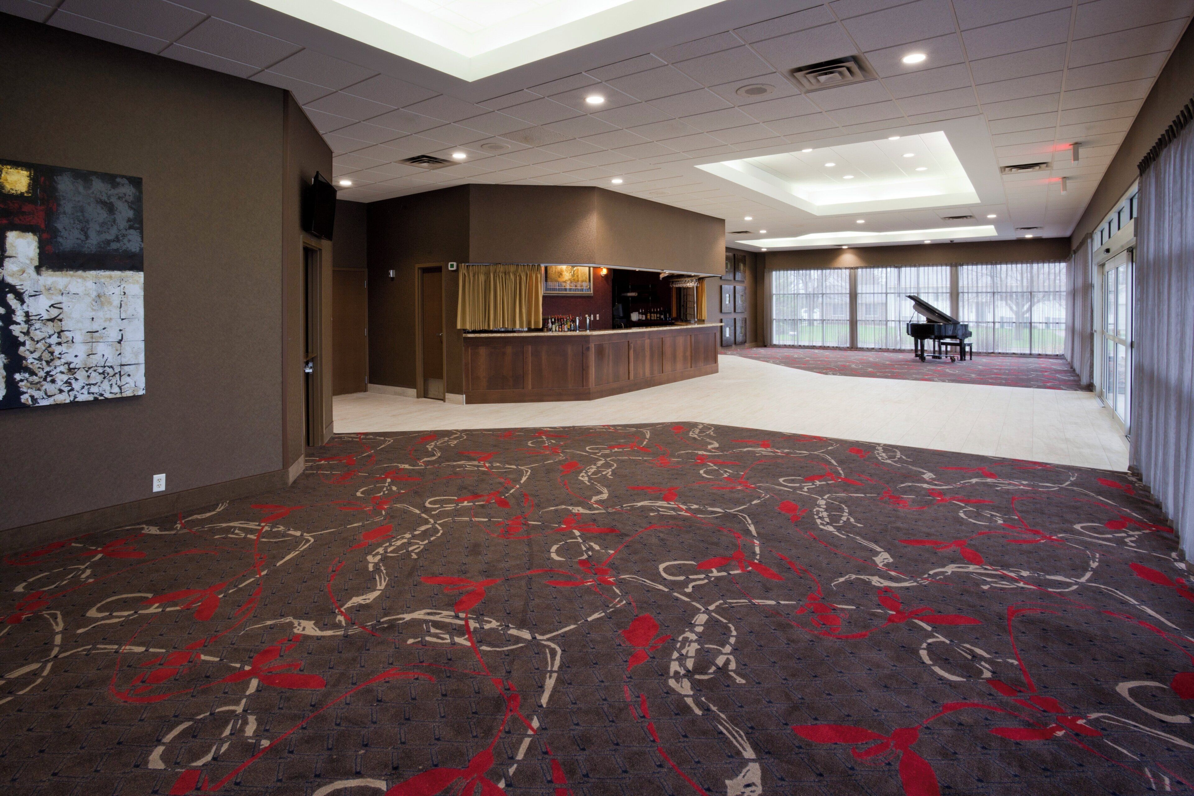 Un vestíbulo de hotel con área de bar, un piano de cola y alfombra estampada.