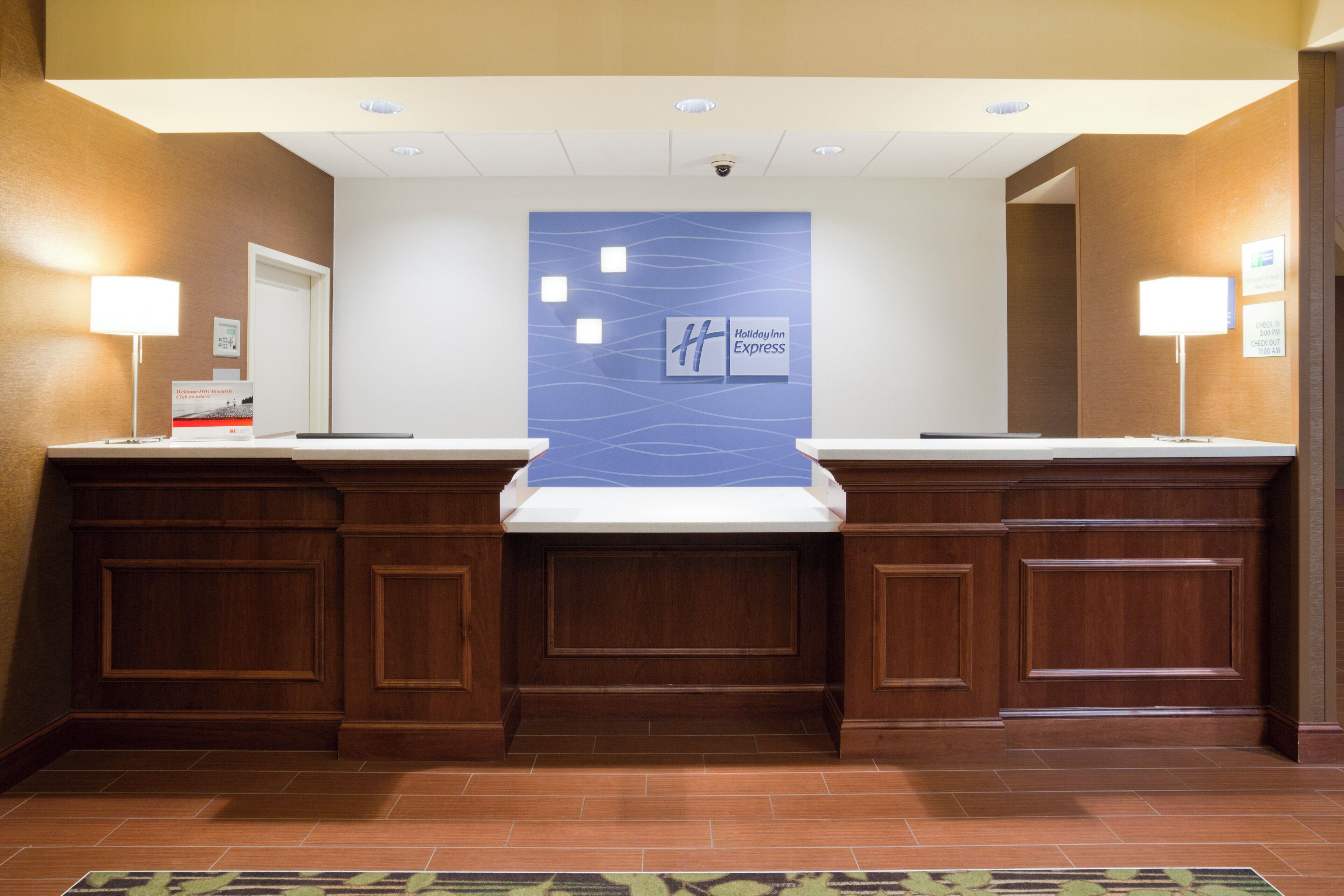 En hotellobby med en central vägg där Holiday Inn Express-logotypen visas, två receptionsdiskar och en övervakningskamera ovanför.