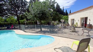 A swimming pool with lounge chairs and tables, surrounded by a fence and trees. - Hôtel du Vieux Moulin (Gignac)