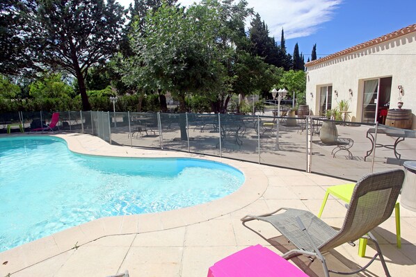 A swimming pool with lounge chairs and tables, surrounded by a fence and trees.