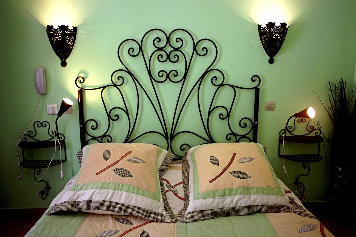 Un lit avec une tête de lit en métal, deux lampes fixées au mur et une table de chevet avec une lampe.