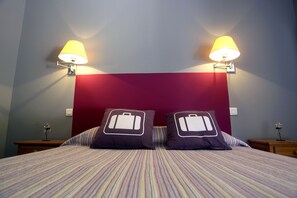 Una habitación de hotel con una cama, dos lámparas de noche, un cabecero rojo y dos almohadas con diseño de maleta.