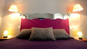 A bed with a purple quilt, two bedside lamps, and a mirror above the bed. - Hôtel du Vieux Moulin (Gignac)
