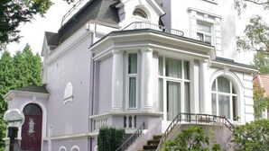 A two-story house with a prominent front entrance, a staircase leading to the upper floor, and a balcony on the second floor. - Hotel Schmidt (Hamburg)
