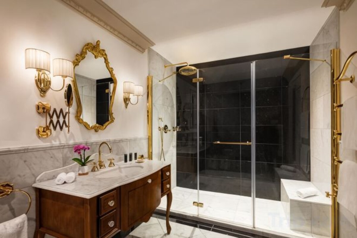 Un bagno lussuoso con un elegante mobile lavabo in marmo, un ampio specchio con luci decorative, una cabina doccia in vetro e un pavimento piastrellato in marmo.