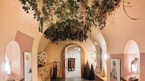 Un pasillo con decoración rústica y terrosa, que incluye un carro de madera con una vela y una bandeja de nueces, una maleta antigua y un árbol de Navidad.