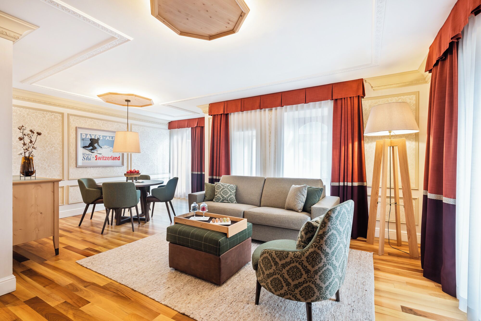 Un salón luminoso con sofá, sillón y mesa de centro. Se observa una zona de comedor con sillas y una mesa, y una lámpara.