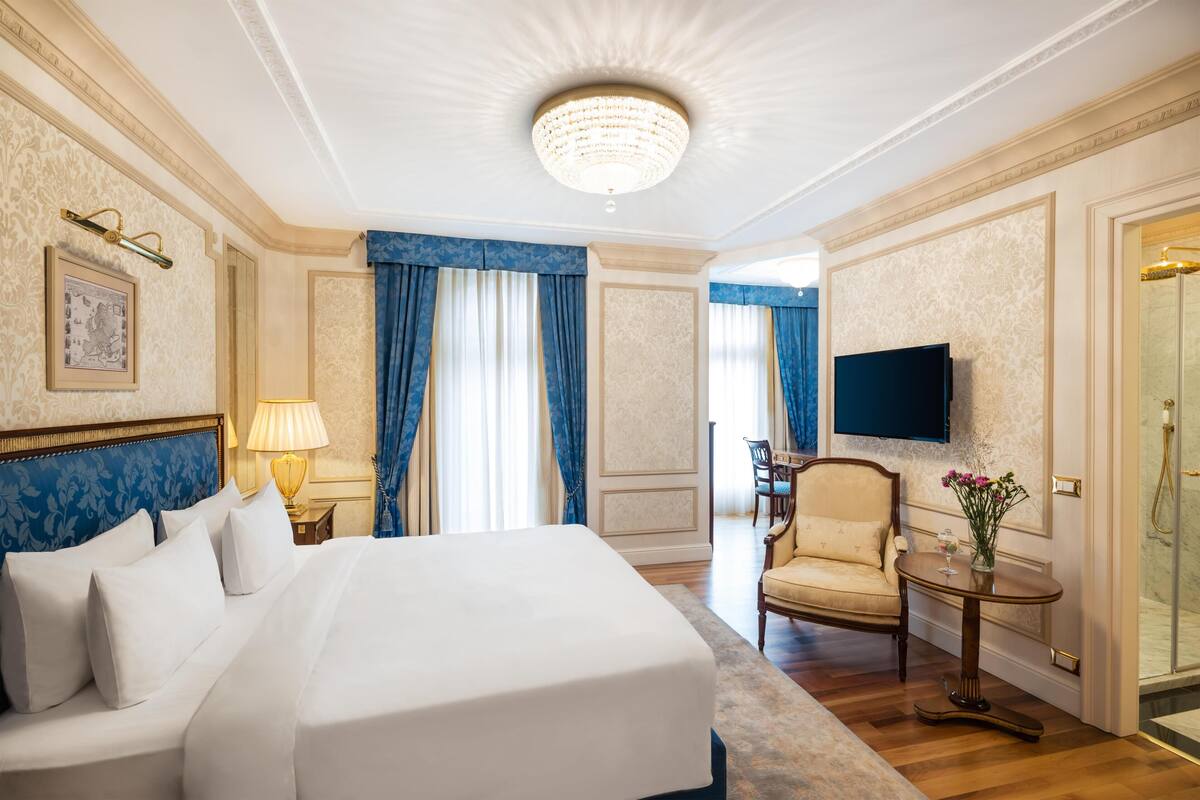 Ett hotellrum med en stor säng, en tv, en stol och ett litet bord med en vas med blommor.