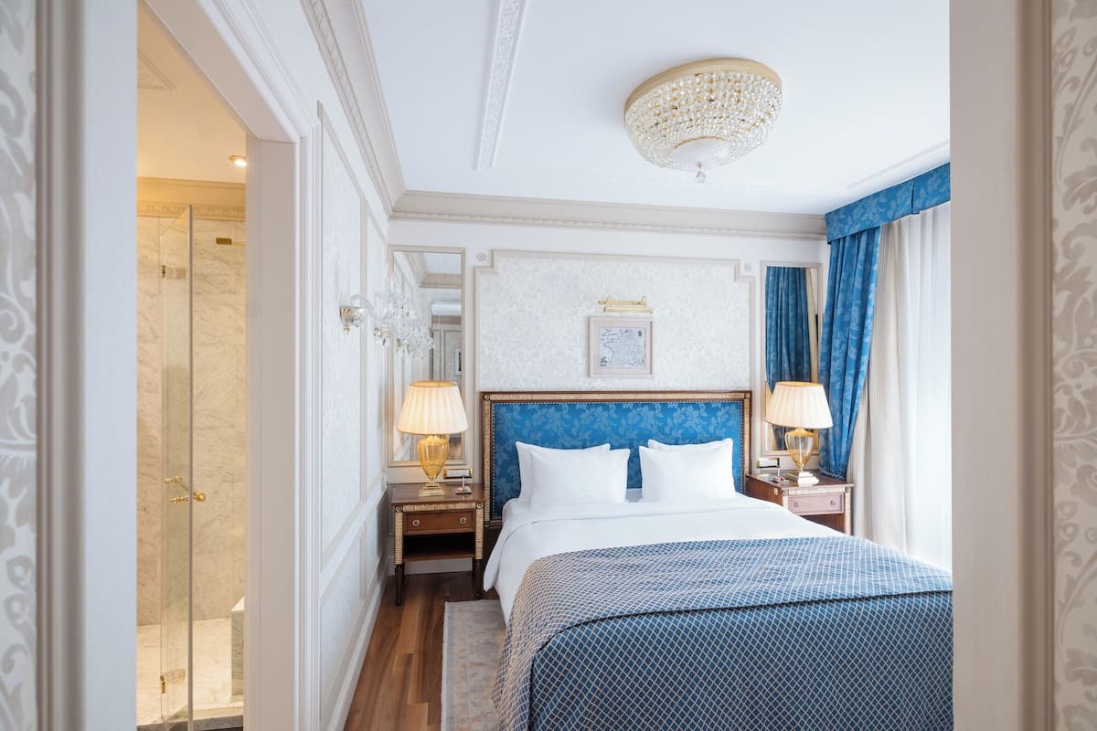 Ett hotellrum med en stor säng, två sängbord med lampor, en stor spegel och en kristallkrona.