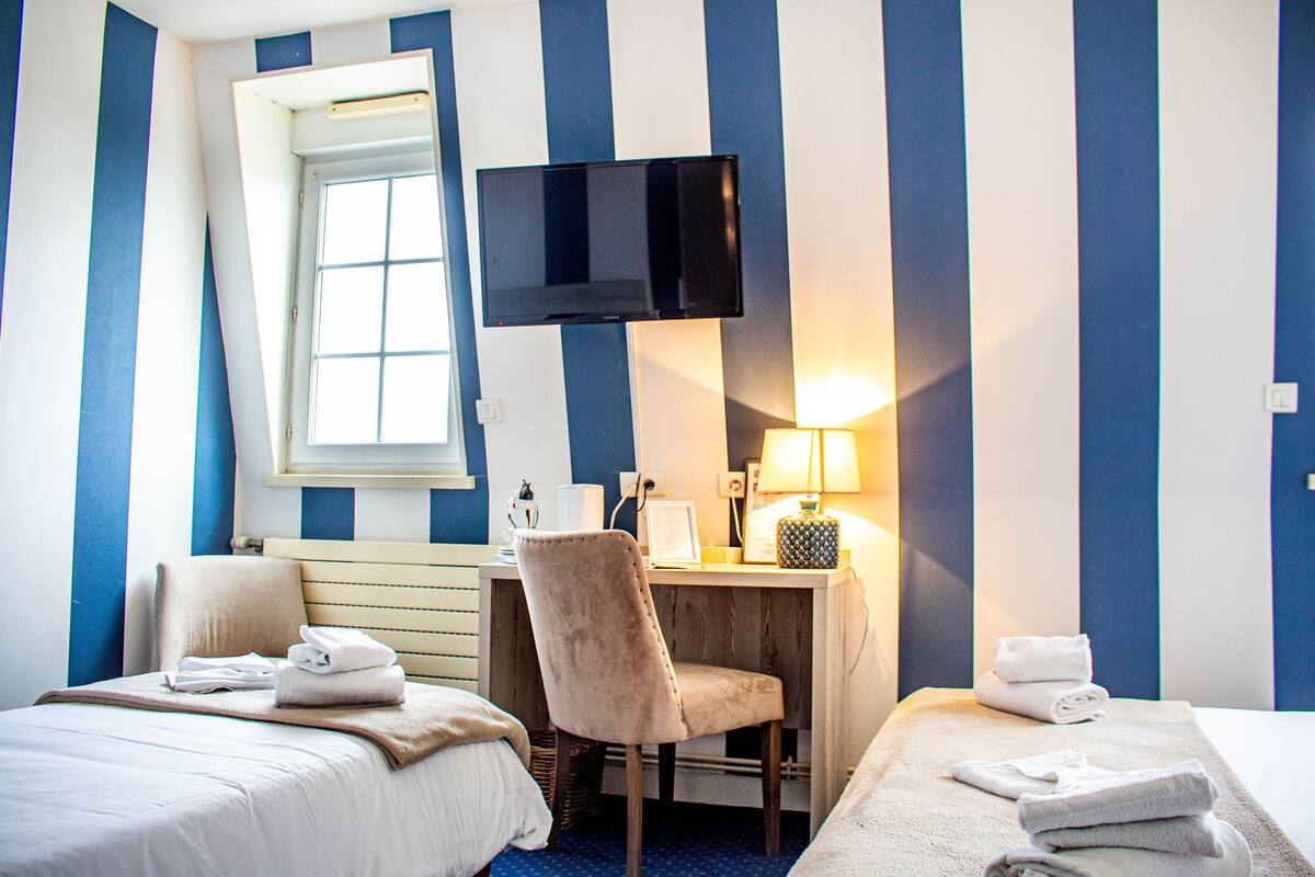 A hotel room with two beds, a desk, a TV, and a window.