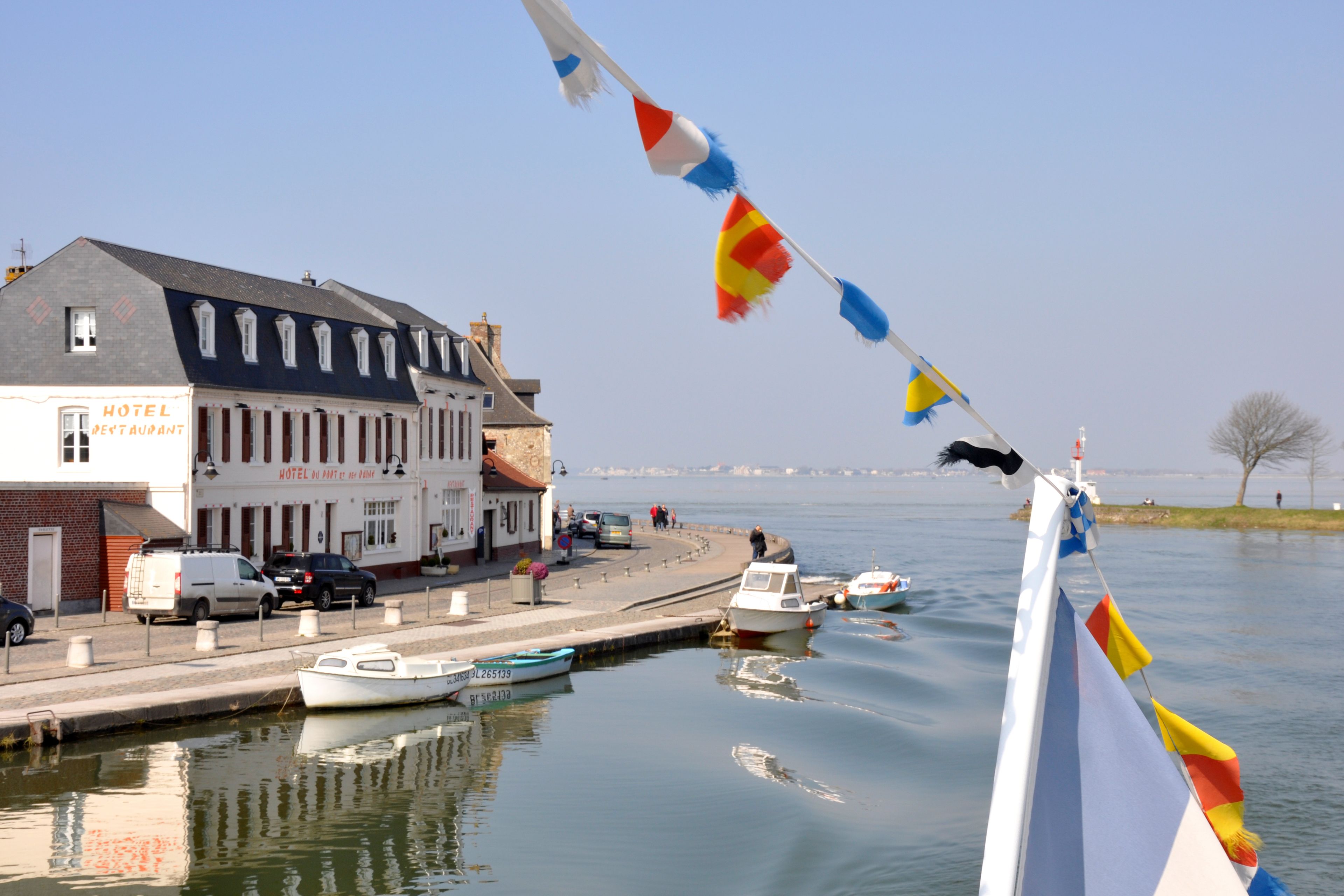 A hotel with a sign indicating it is a restaurant, located by a calm body of water with boats docked.