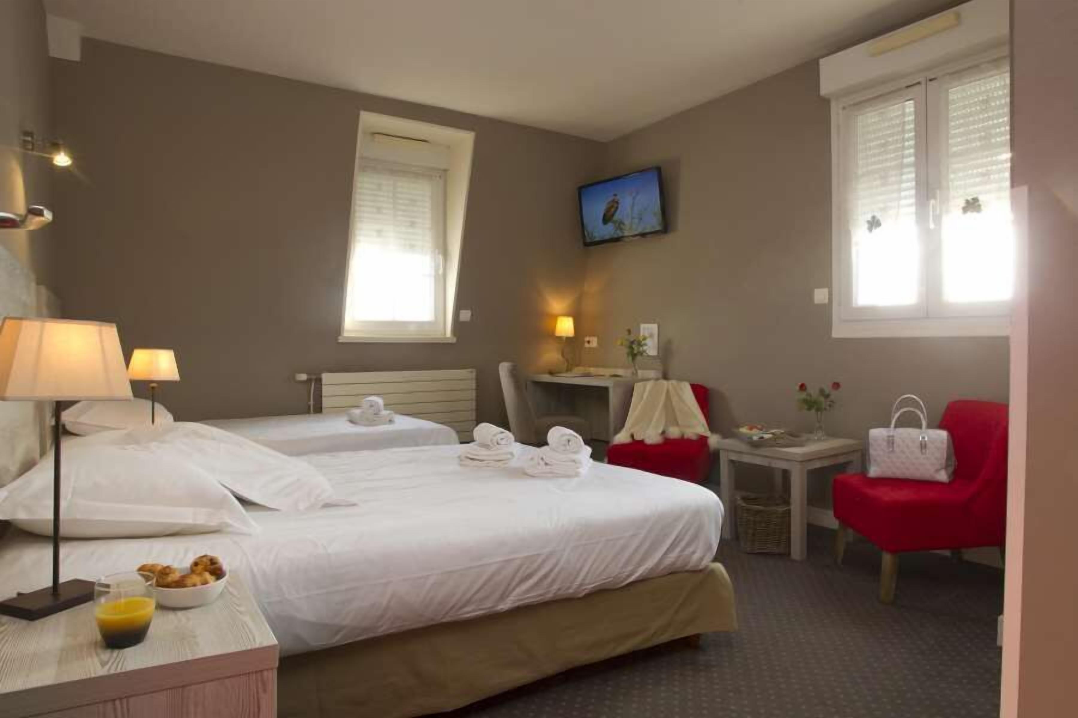 Een hotelkamer met twee bedden, een bureau, een stoel en een televisie aan de muur.