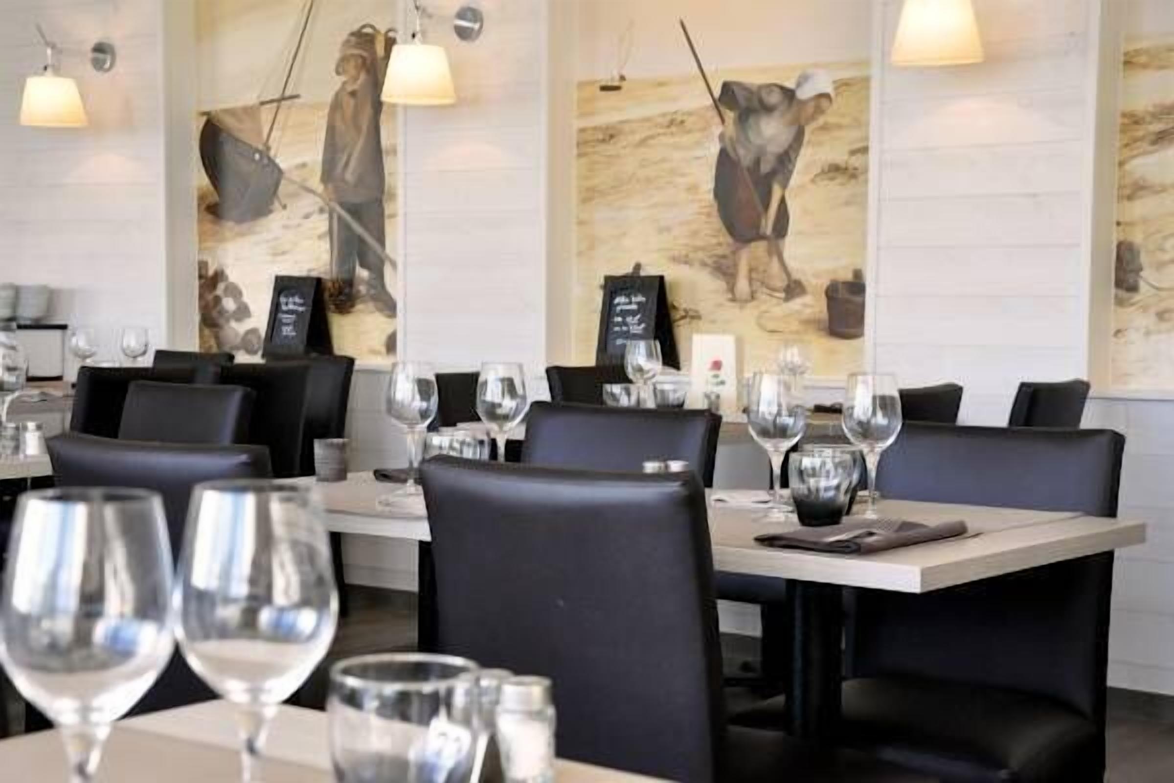 A restaurant interior with tables set for dining, featuring artwork on the walls and pendant lighting.