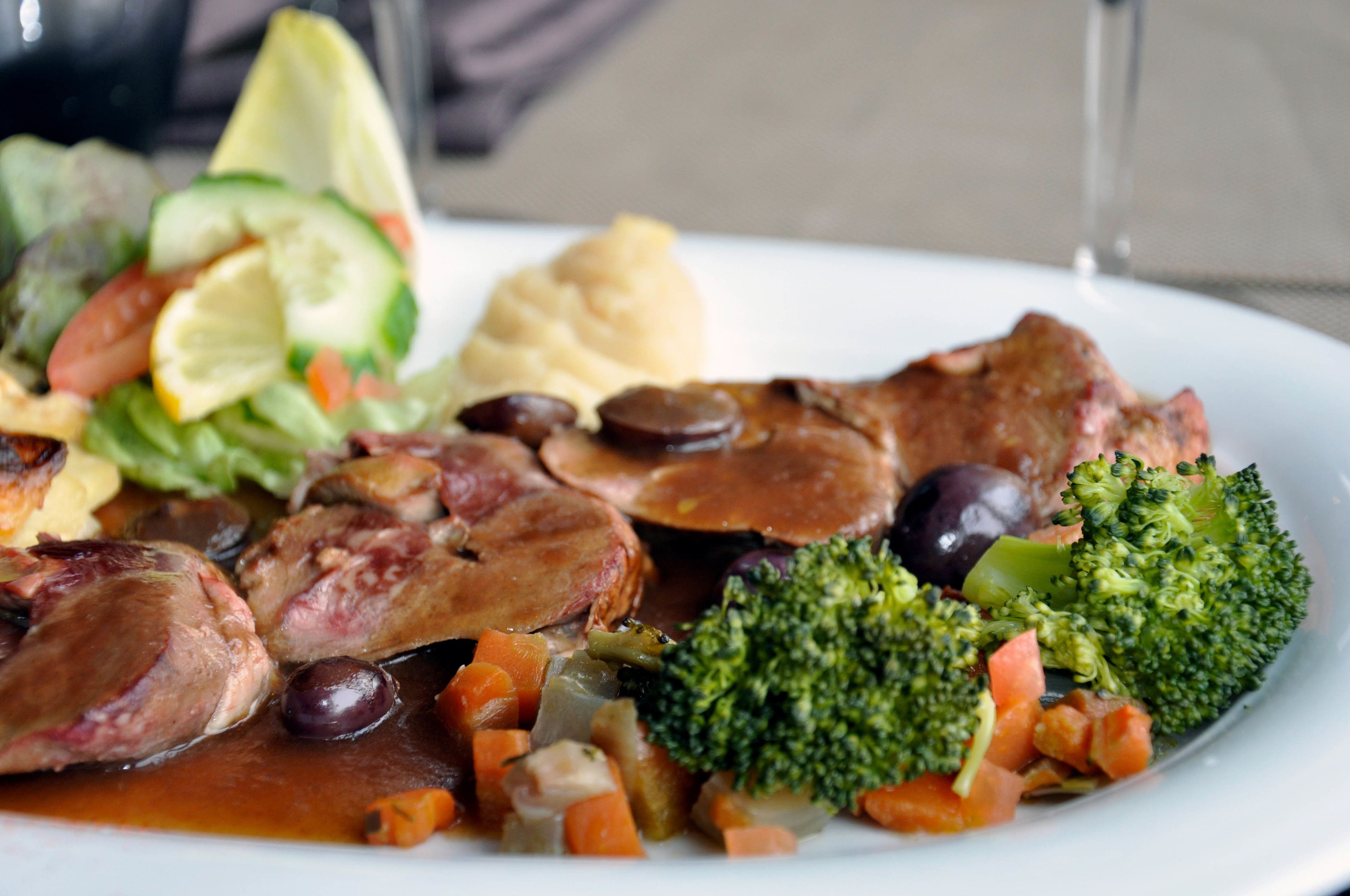 A plate of food with meat, vegetables, and a slice of lemon.