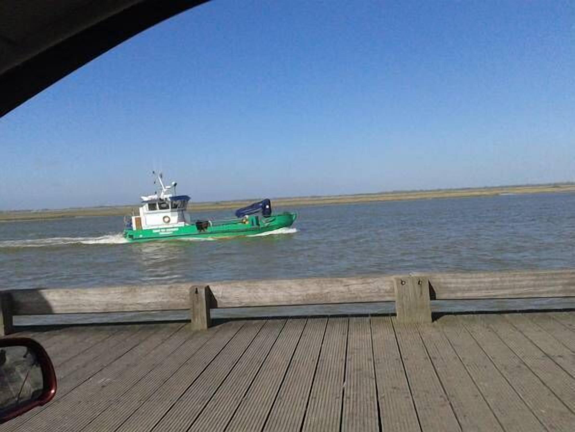 Un bote verde sobre el agua, visto desde una cubierta de madera.