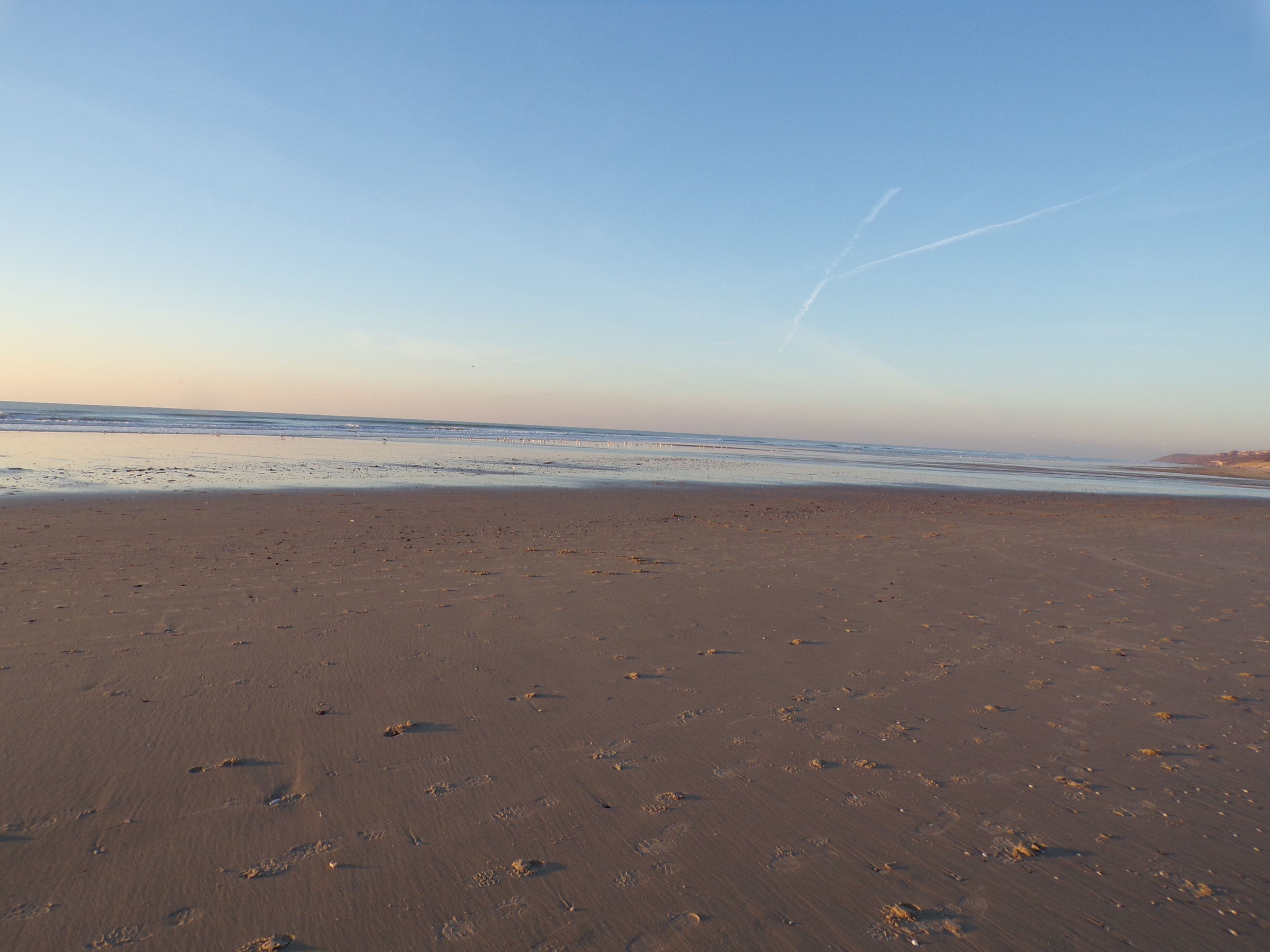 A wide sandy beach with footprints and a clear sky.
