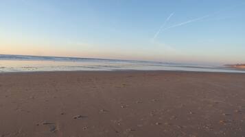A wide sandy beach with footprints and a clear sky.