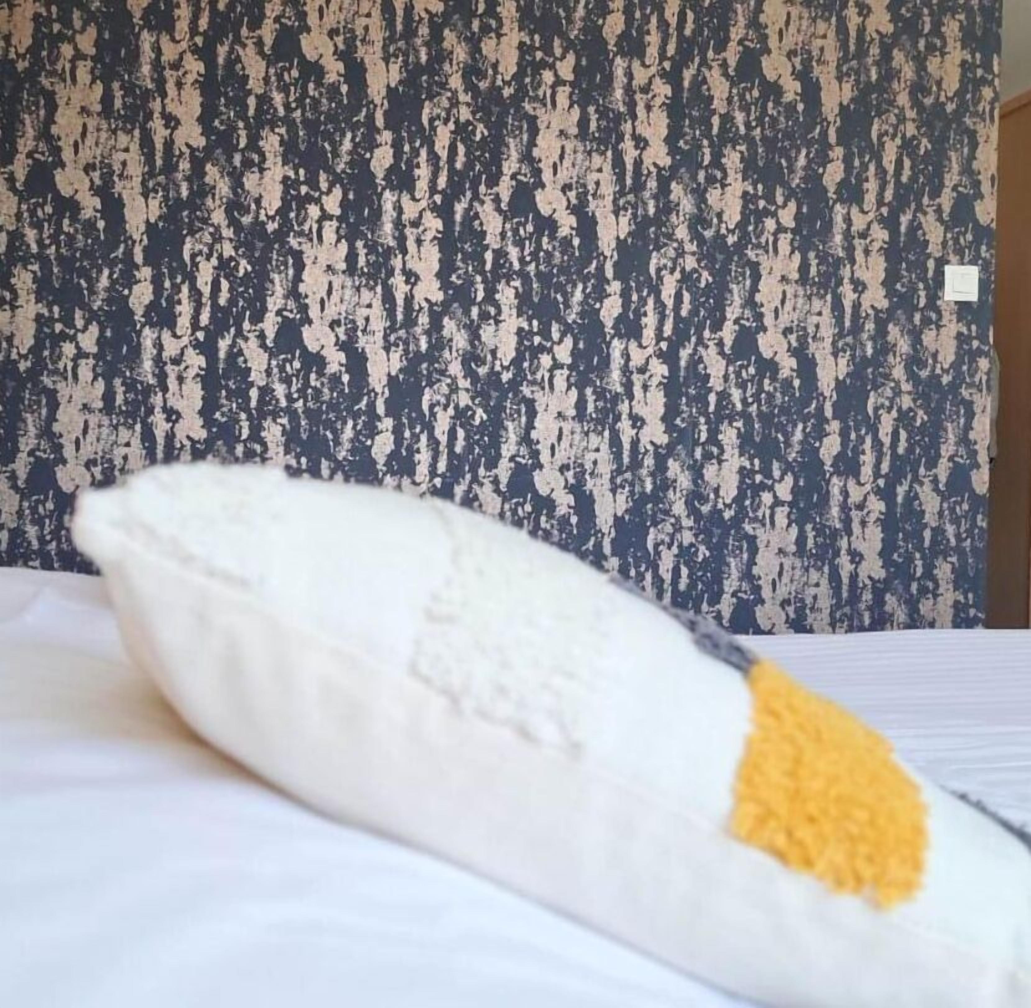 Almohada blanca con un detalle amarillo sobre una cama frente a una pared con textura.