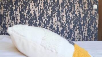 Almohada blanca con un detalle amarillo sobre una cama frente a una pared con textura.