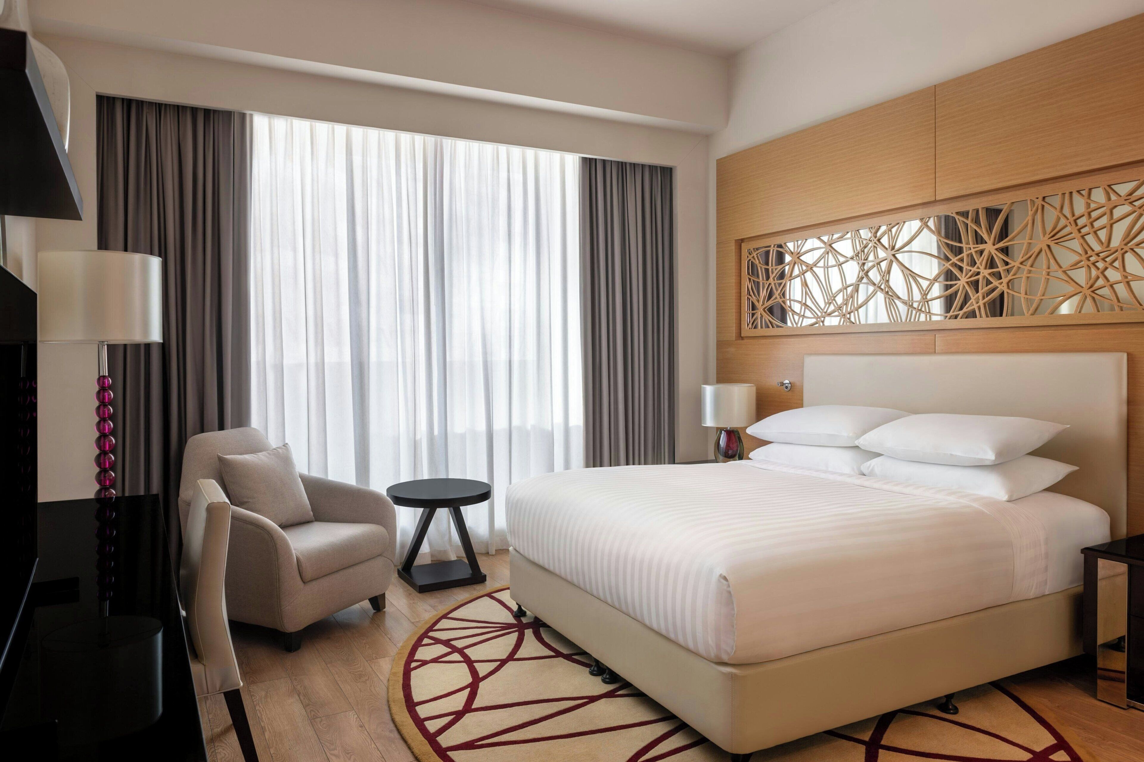 A hotel room with a large bed, a chair, a small table, and a TV.