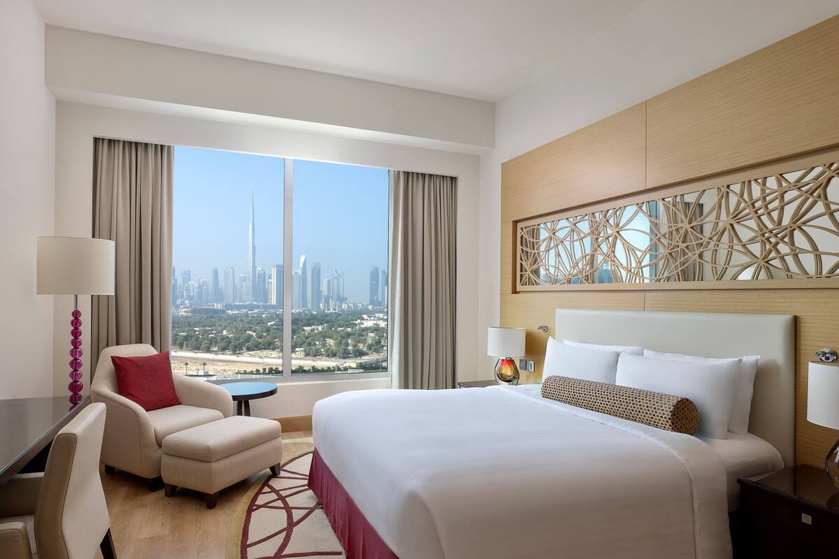 A hotel room with a large bed, a desk, a chair, and a view of a cityscape.