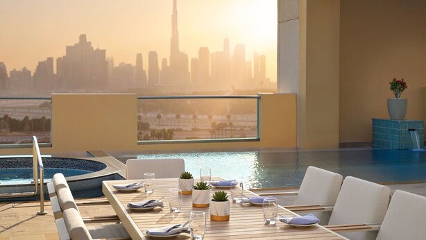Zona de piscina en la azotea con mesa lista para comer, con vistas a un horizonte urbano.