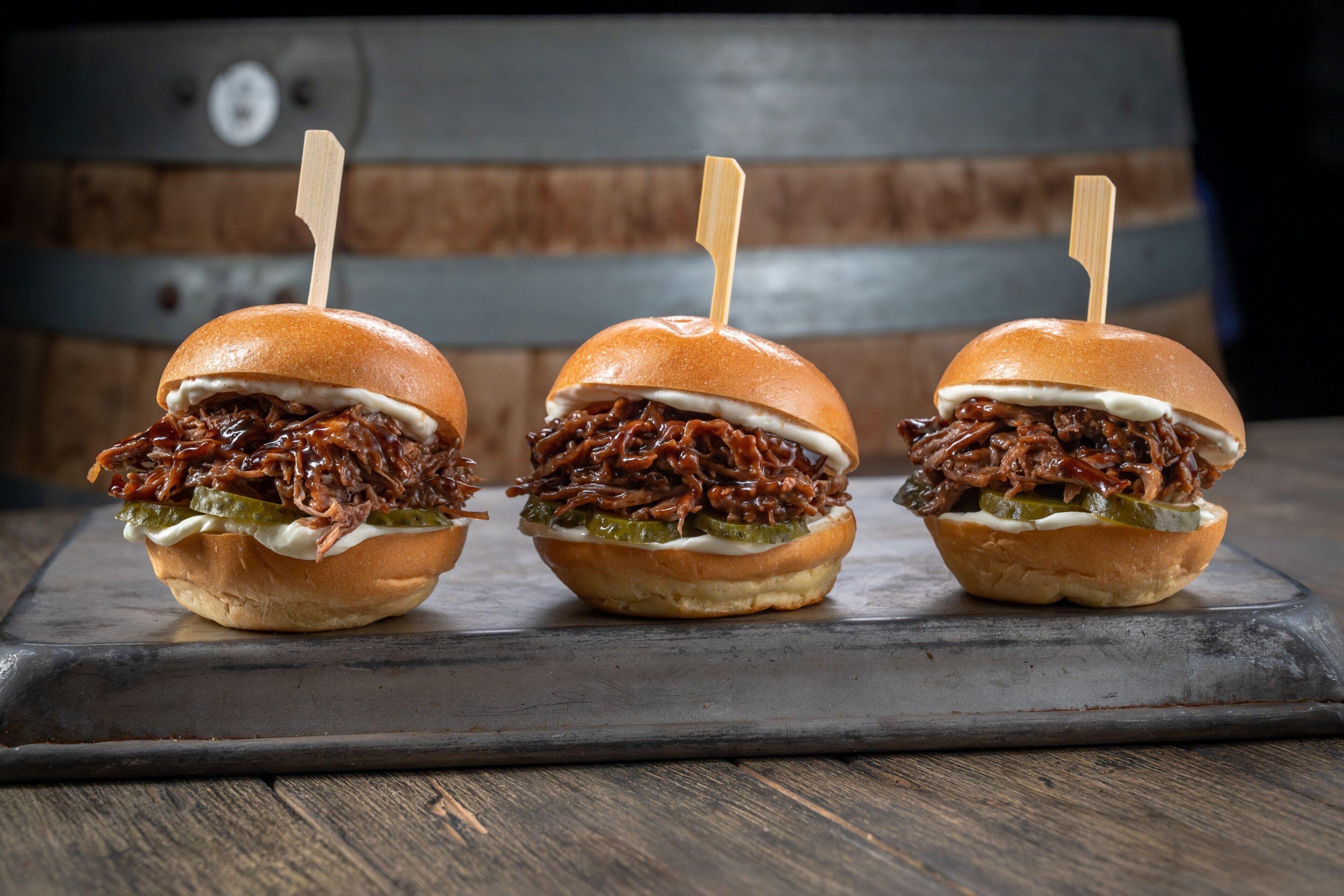 Three pulled pork sliders on a wooden board.
