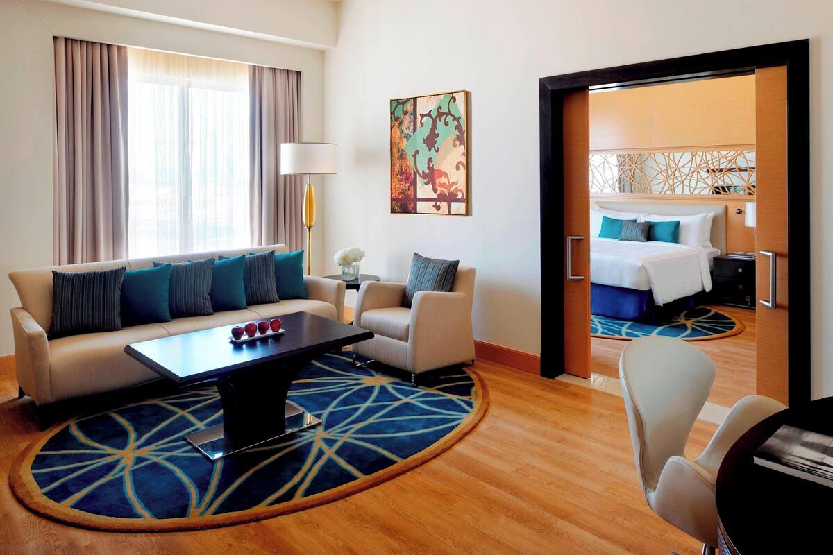 A hotel room with a sofa, armchair, and a bed with a headboard.