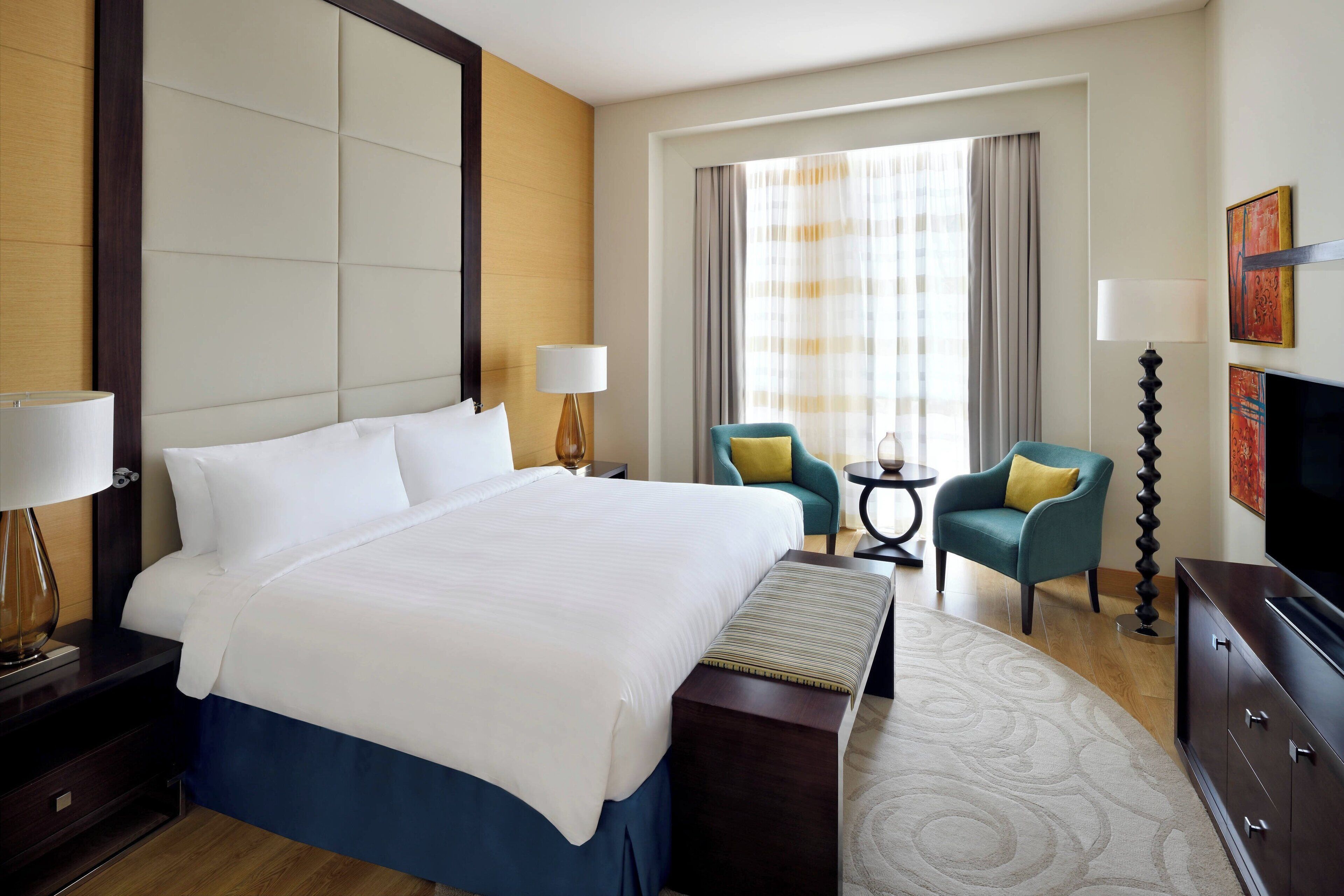 A hotel room with a large bed, two armchairs, a television, and a small table with lamps.
