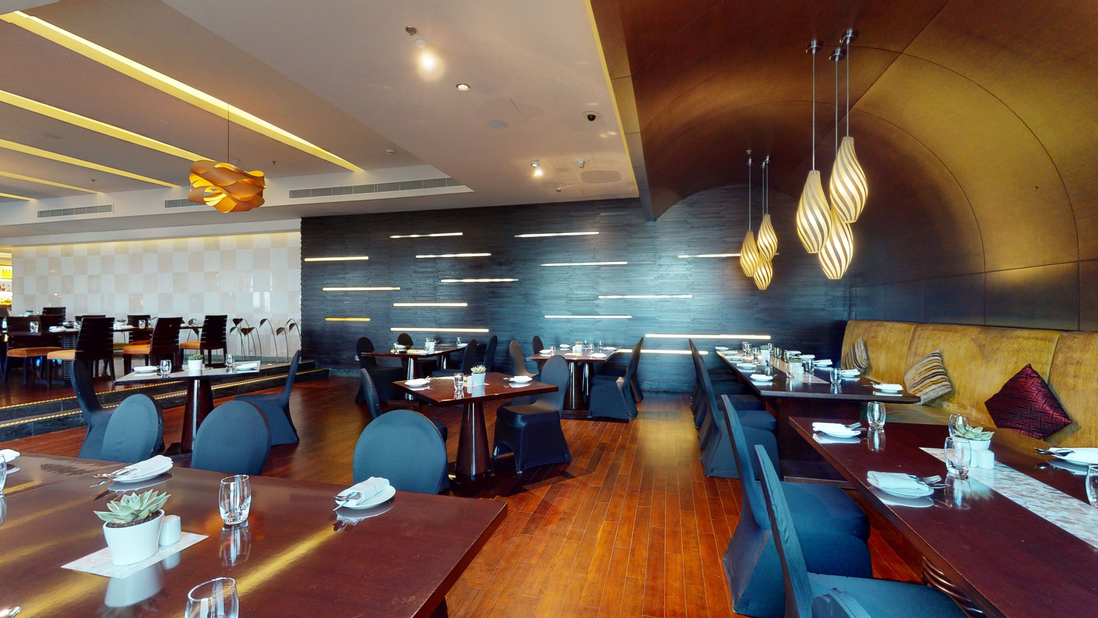 A modern restaurant interior with long tables, dark wood flooring, and contemporary lighting fixtures.