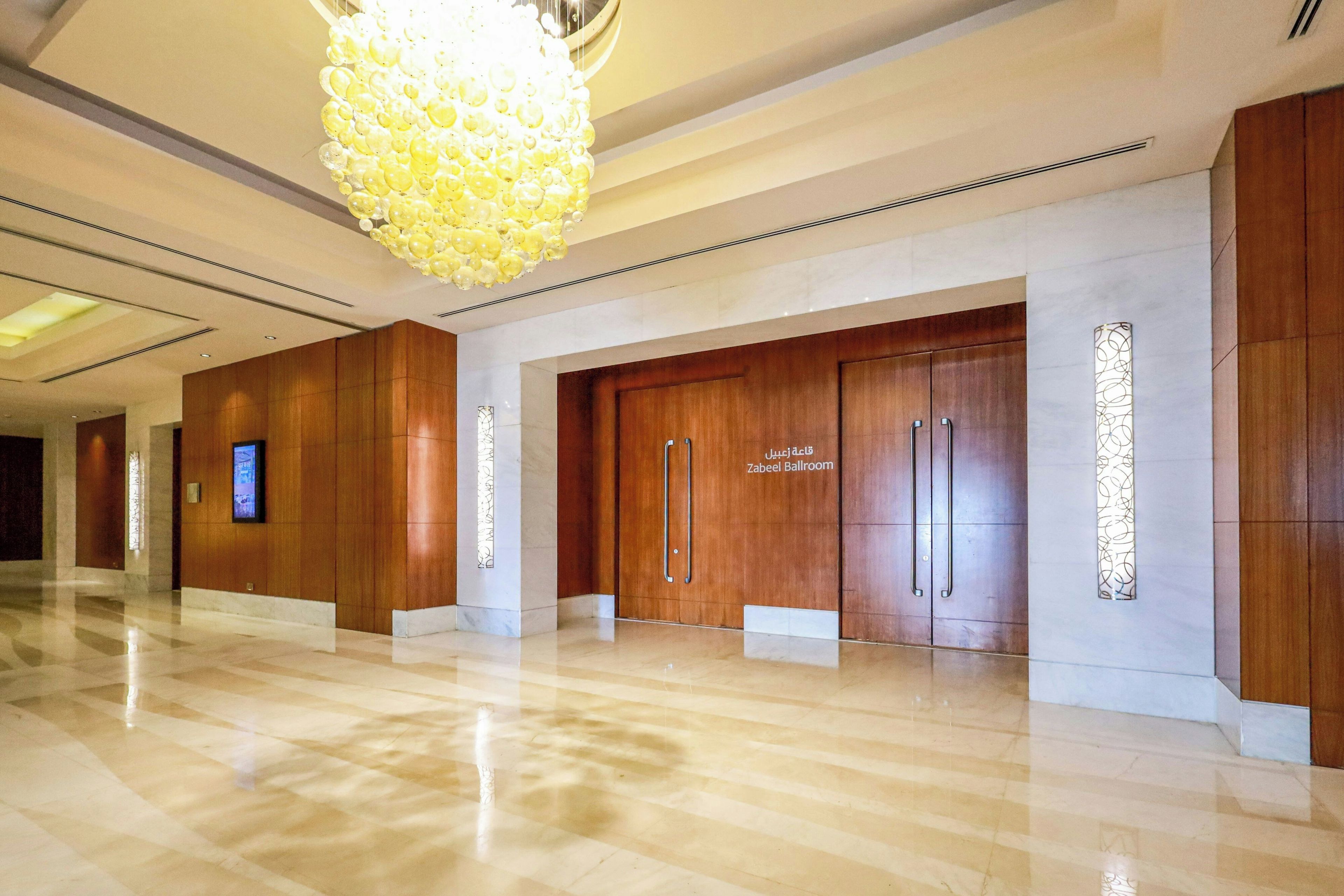 Un'hall dell'hotel con pavimento in marmo lucidato, un grande lampadario e porte in legno con la scritta 'Zabeel Ballroom'.