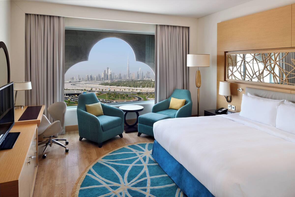A hotel room with a large bed, two armchairs, a desk, and a view of a cityscape.