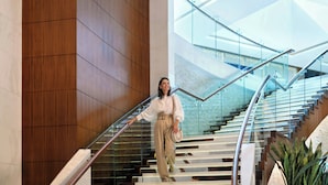 Un interior moderno con una escalera de cristal, paneles de madera y un elemento decorativo de iluminación.