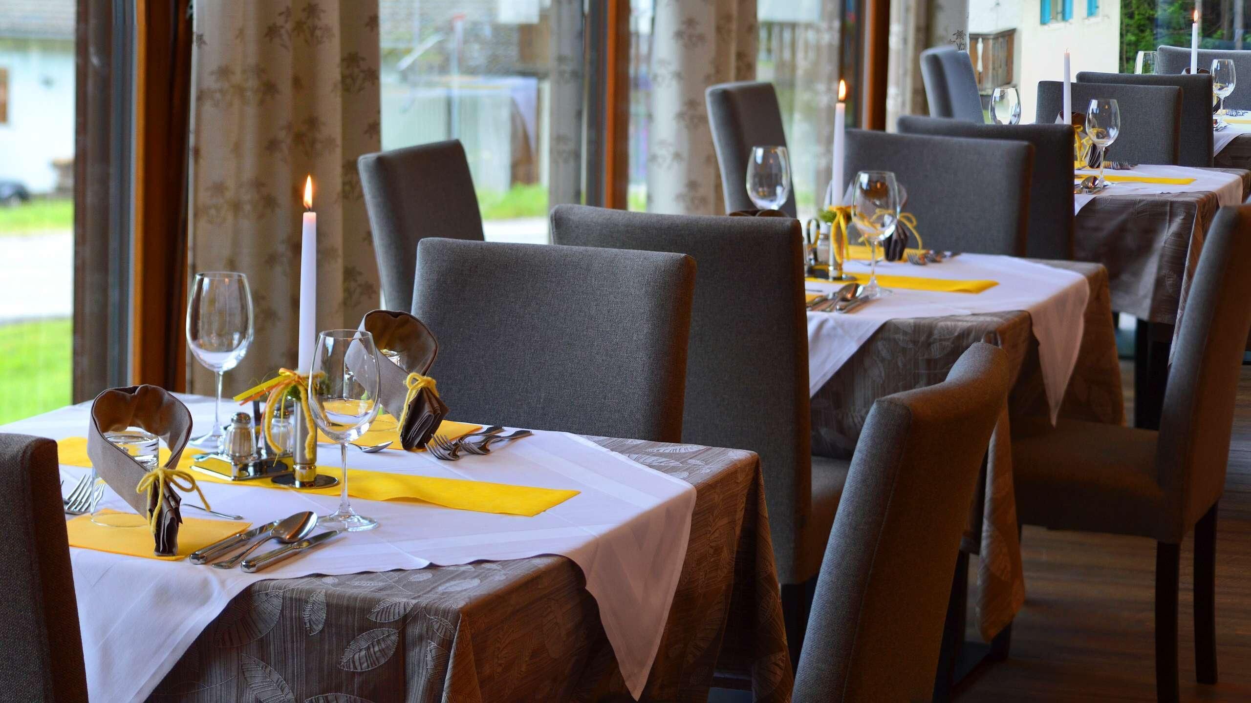 A restaurant with tables set for dining, featuring a candle on each table and a view of the outdoors.