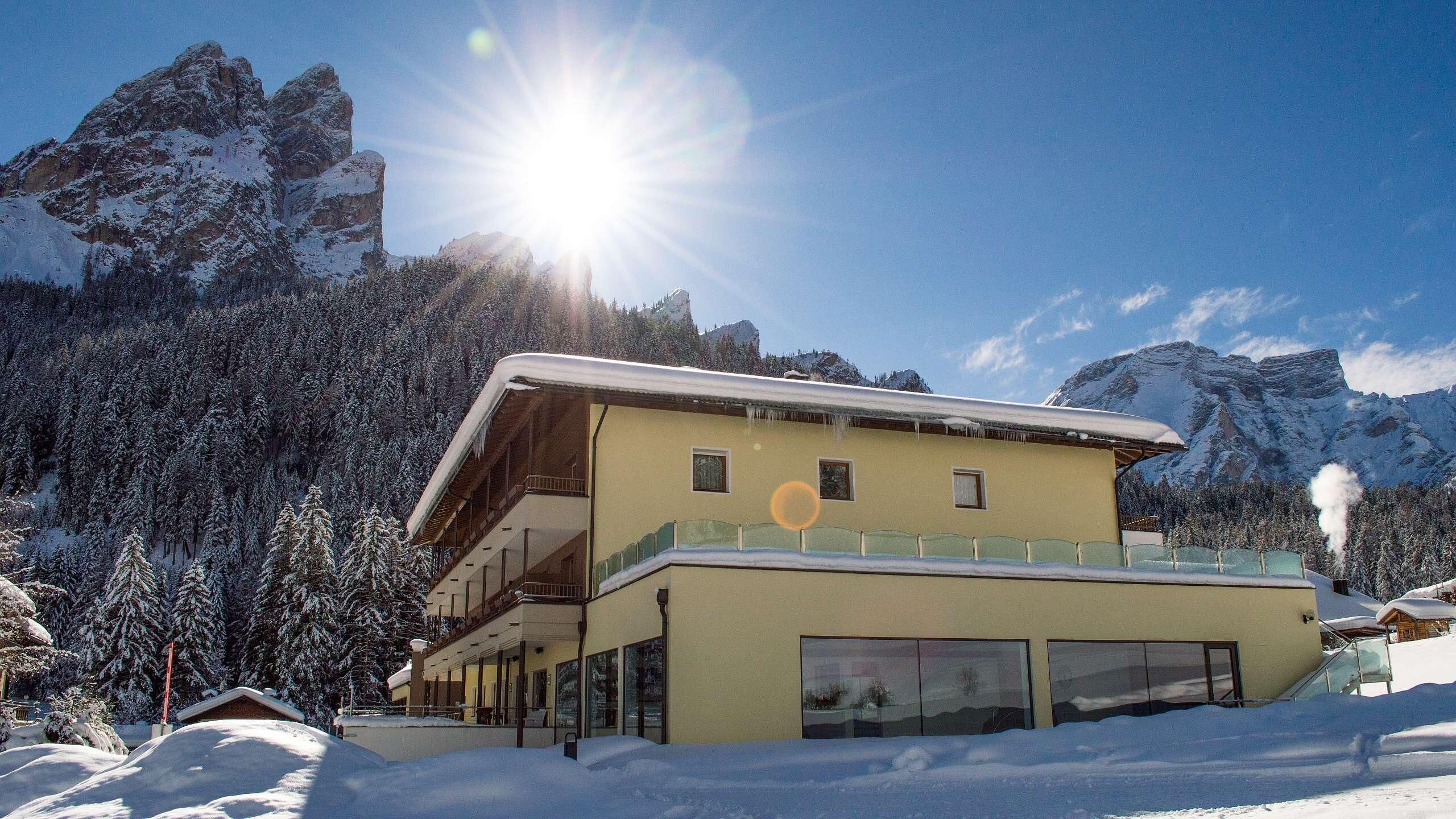 Um edifício de dois andares com varanda, cercado por árvores e montanhas cobertas de neve.