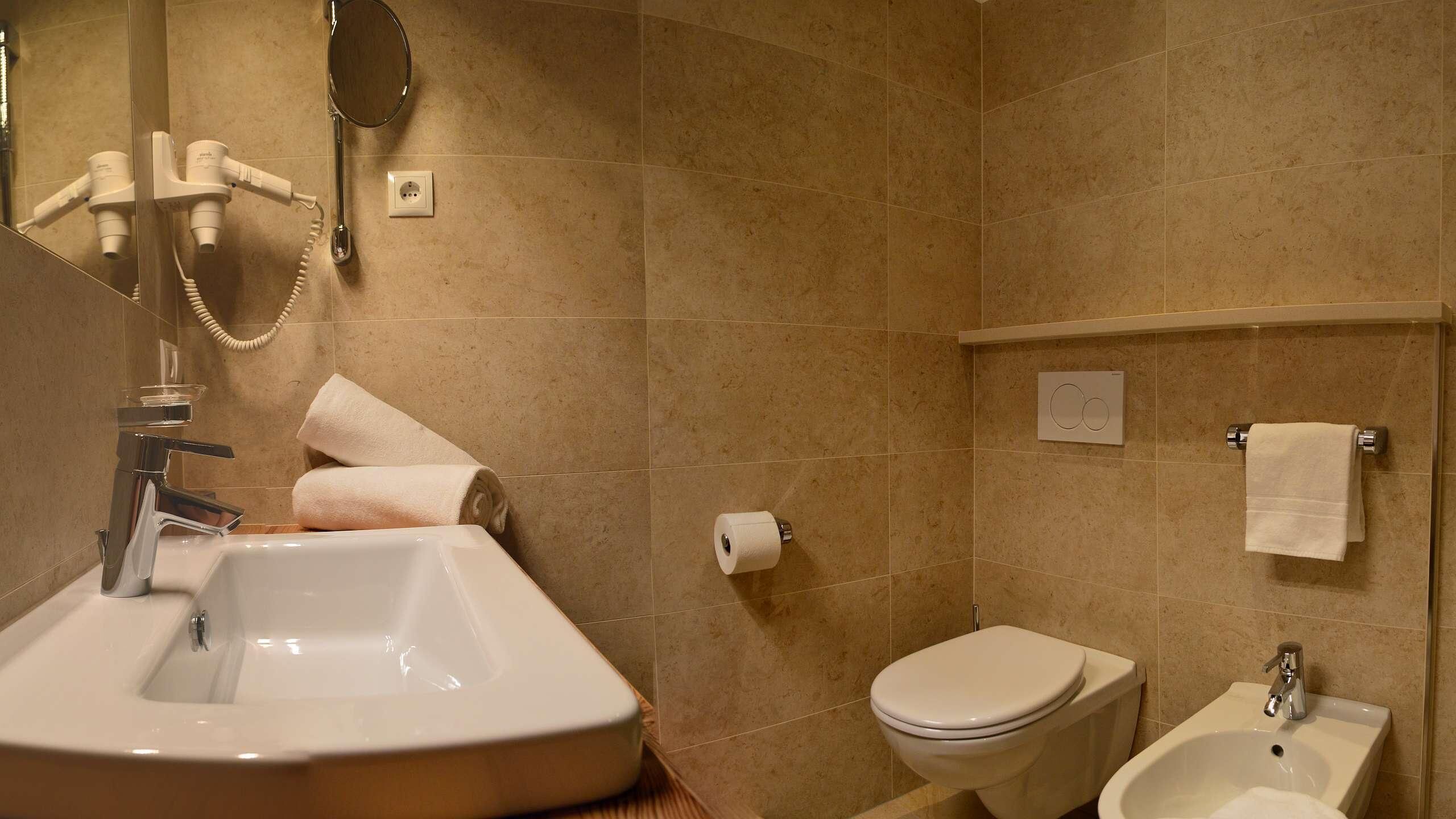 A bathroom with a sink, toilet, bidet, and towel rack.