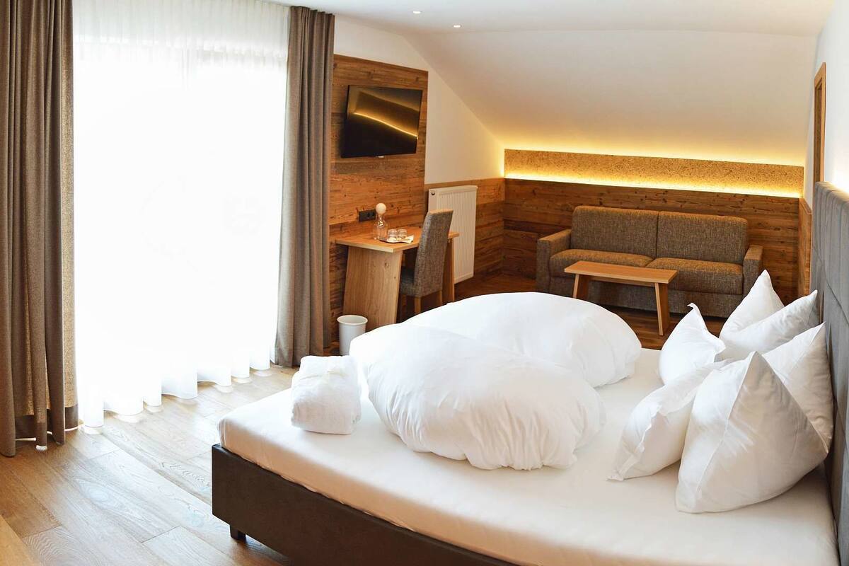 A modern hotel room with a large bed, a seating area with a sofa and table, and a television mounted on the wall.