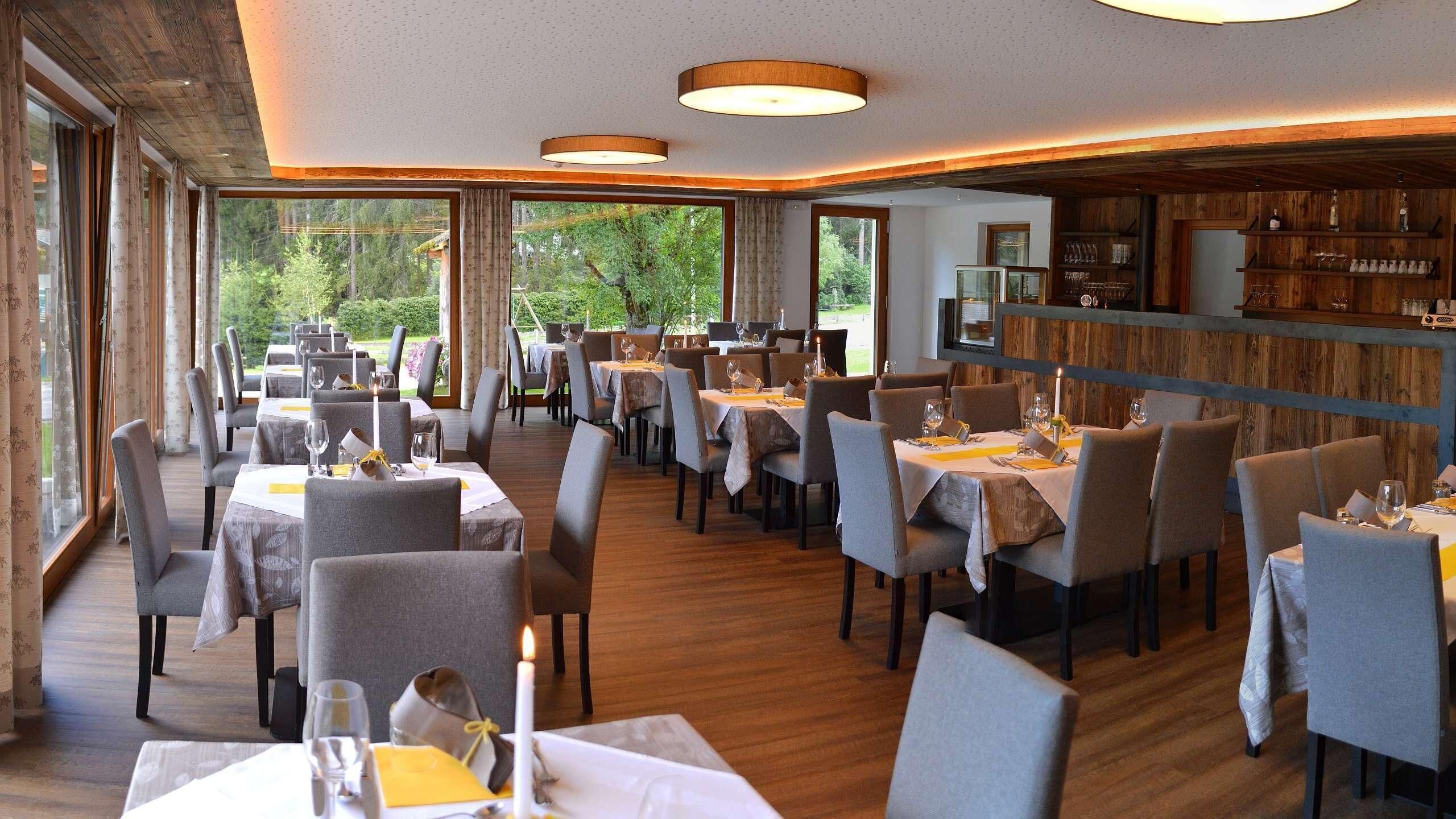 Un restaurante con mesas dispuestas para comer, ventanas amplias y decoración de madera.