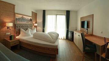 A hotel room with a bed, a desk, a chair, a TV, and a painting on the wall.